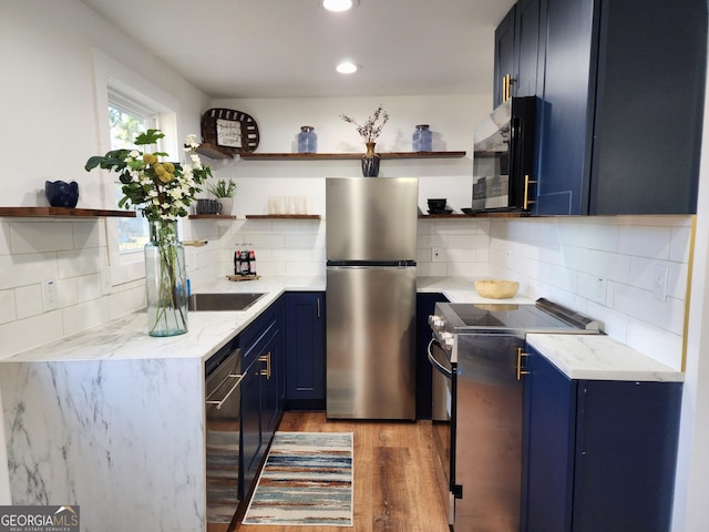 kitchen featuring light stone countertops, light hardwood / wood-style flooring, backsplash, blue cabinetry, and appliances with stainless steel finishes