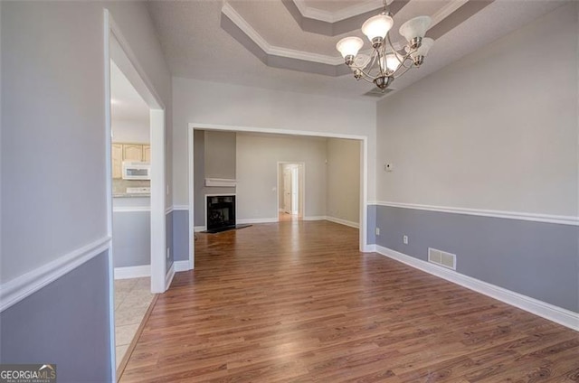 unfurnished dining area featuring hardwood / wood-style floors, a notable chandelier, ornamental molding, and a tray ceiling