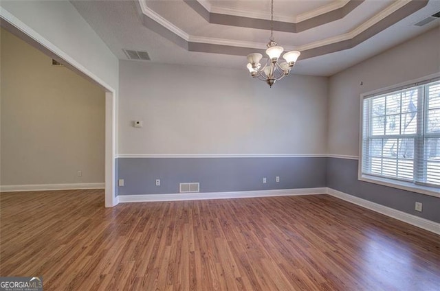 empty room with a notable chandelier, a raised ceiling, wood-type flooring, and ornamental molding