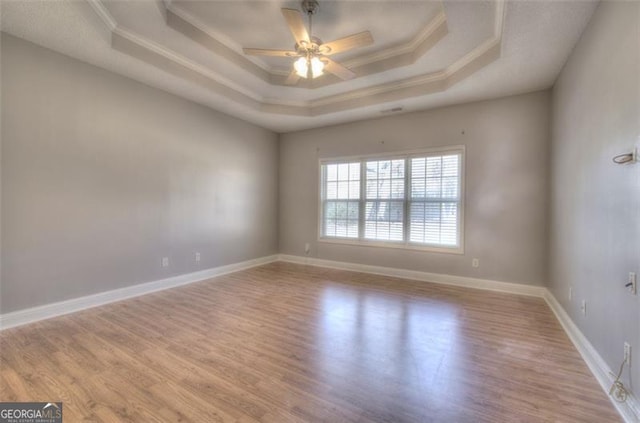 spare room featuring a tray ceiling, ceiling fan, light hardwood / wood-style flooring, and ornamental molding