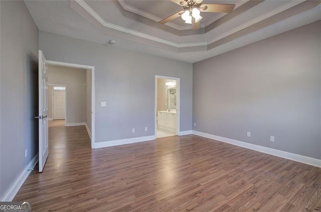 spare room featuring a raised ceiling, ceiling fan, wood-type flooring, and ornamental molding