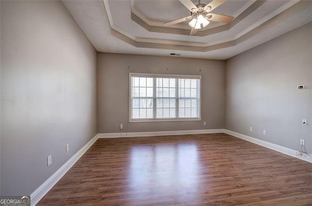 unfurnished room featuring a tray ceiling, dark hardwood / wood-style floors, ornamental molding, and ceiling fan