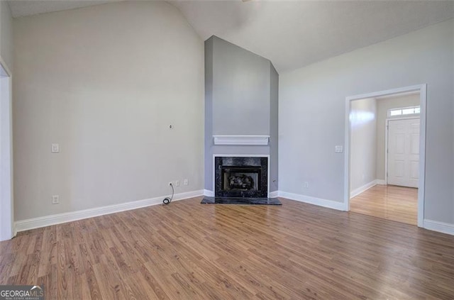 unfurnished living room featuring hardwood / wood-style floors, lofted ceiling, and a high end fireplace