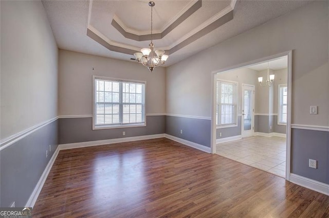 unfurnished room featuring a tray ceiling, an inviting chandelier, hardwood / wood-style flooring, and ornamental molding