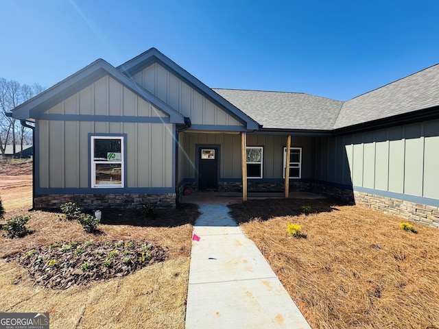 view of front of property with board and batten siding, stone siding, covered porch, and a shingled roof