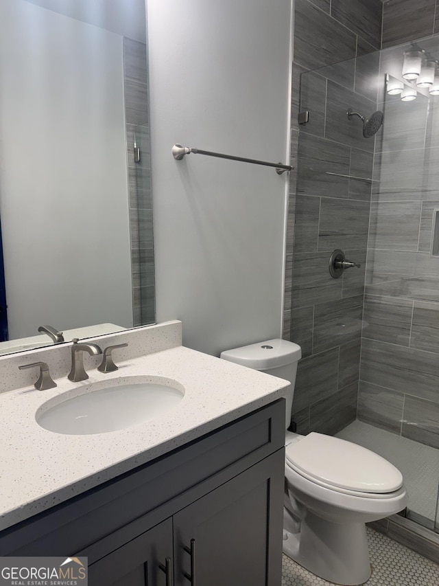 bathroom with tile patterned floors, toilet, a tile shower, and vanity