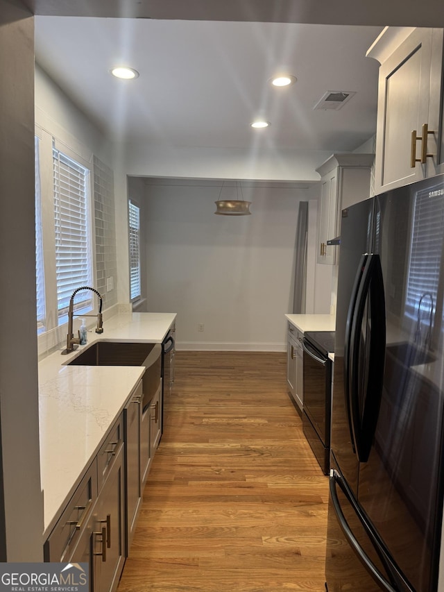 kitchen featuring light stone countertops, sink, light hardwood / wood-style floors, decorative light fixtures, and black appliances