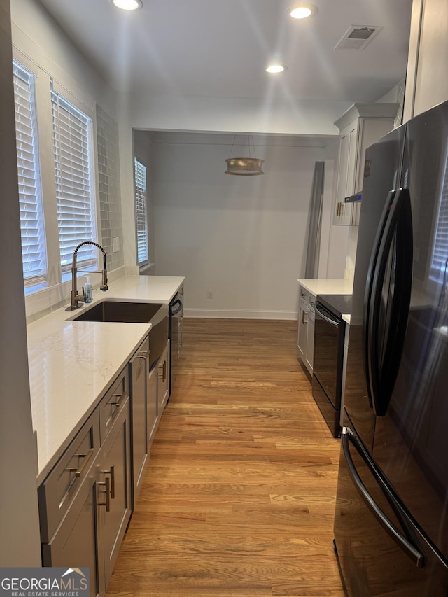 kitchen featuring light stone countertops, sink, light hardwood / wood-style flooring, black electric range, and stainless steel refrigerator