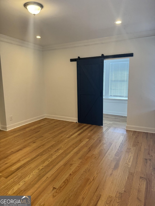 empty room with hardwood / wood-style floors, a barn door, and ornamental molding