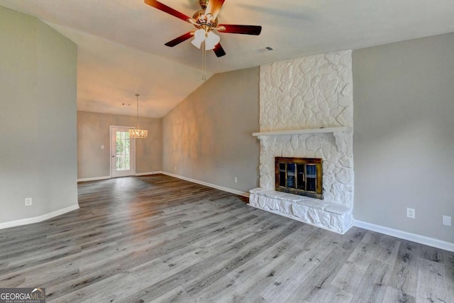 unfurnished living room with ceiling fan with notable chandelier, a stone fireplace, wood-type flooring, and vaulted ceiling