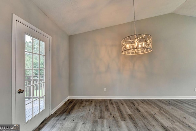 unfurnished dining area with hardwood / wood-style floors, a chandelier, and vaulted ceiling