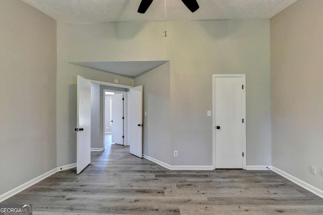 empty room featuring ceiling fan, a towering ceiling, a textured ceiling, and light wood-type flooring