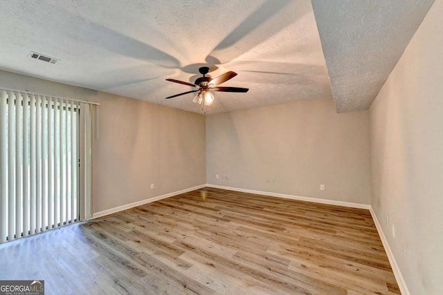 empty room with ceiling fan, light wood-type flooring, and a textured ceiling