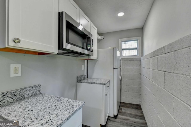 kitchen featuring light stone counters, a textured ceiling, white refrigerator, light hardwood / wood-style flooring, and white cabinetry