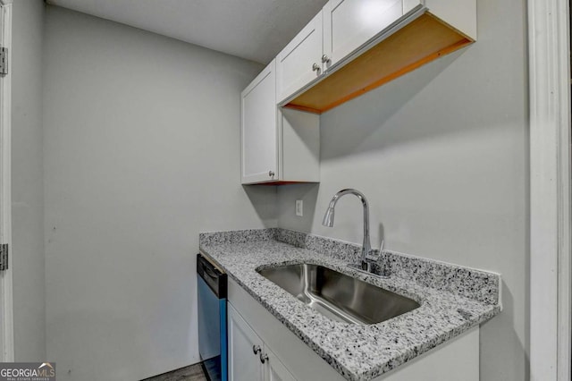 kitchen featuring white cabinetry, sink, stainless steel dishwasher, and light stone counters