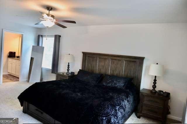 bedroom with connected bathroom, light colored carpet, and ceiling fan