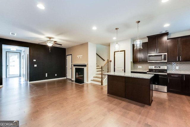 kitchen with a center island, light stone countertops, decorative light fixtures, dark brown cabinets, and stainless steel appliances