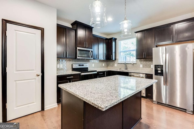 kitchen with light stone counters, dark brown cabinets, stainless steel appliances, decorative light fixtures, and a center island