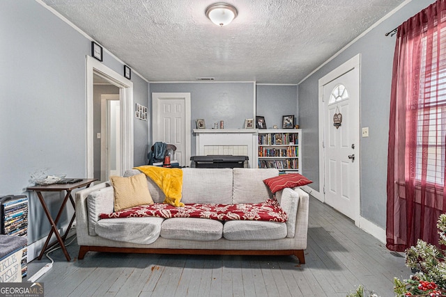 living room with a tile fireplace, crown molding, wood-type flooring, and a textured ceiling