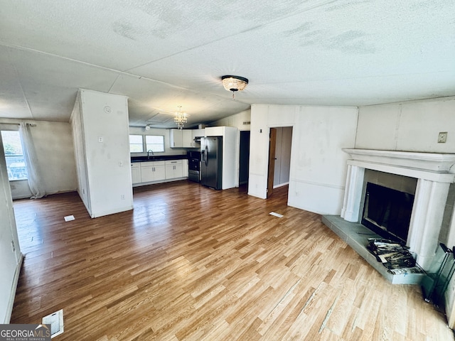 unfurnished living room featuring a textured ceiling, a healthy amount of sunlight, sink, and light hardwood / wood-style flooring