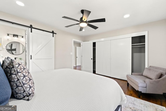 bedroom with ceiling fan, a barn door, and dark wood-type flooring