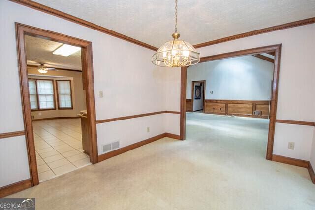 empty room with crown molding, ceiling fan with notable chandelier, light colored carpet, and a textured ceiling