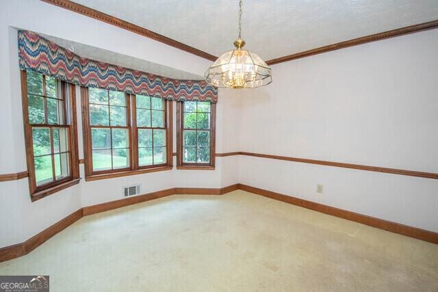 carpeted spare room featuring a notable chandelier and ornamental molding