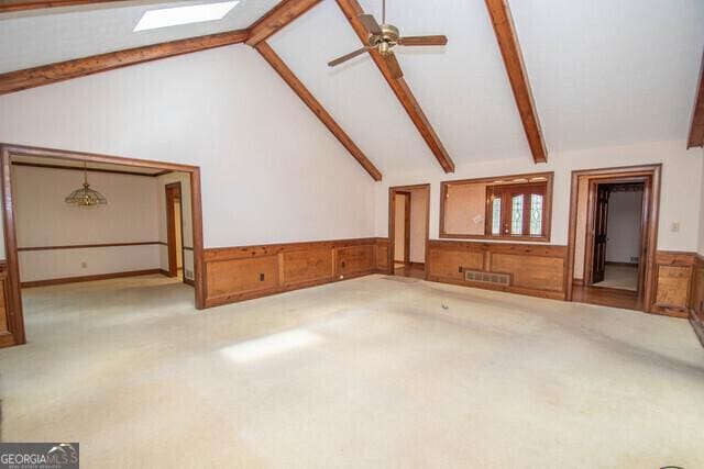 unfurnished living room featuring ceiling fan, vaulted ceiling with skylight, and light colored carpet