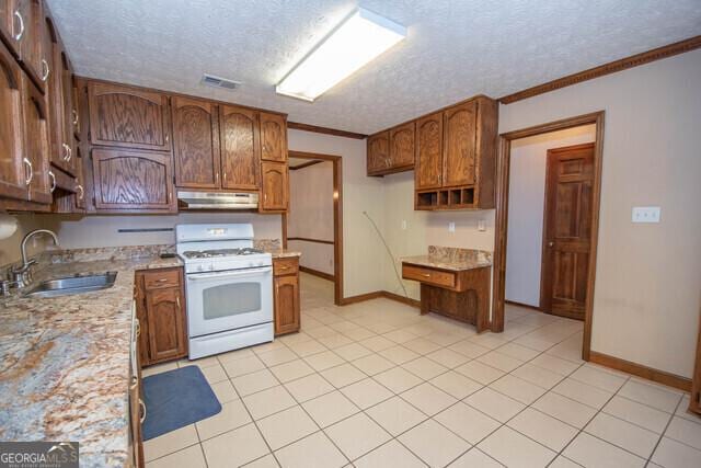 kitchen featuring ornamental molding, a textured ceiling, sink, light tile patterned floors, and white range with gas stovetop