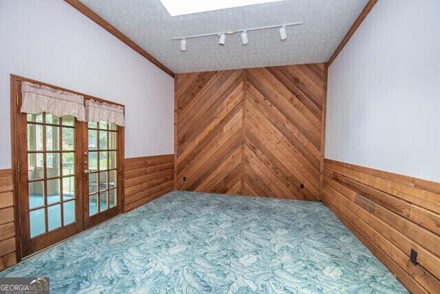 interior space with wood walls, french doors, rail lighting, and a textured ceiling