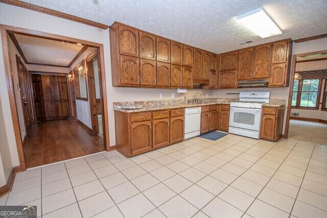 kitchen featuring a textured ceiling, white appliances, light tile patterned floors, and crown molding