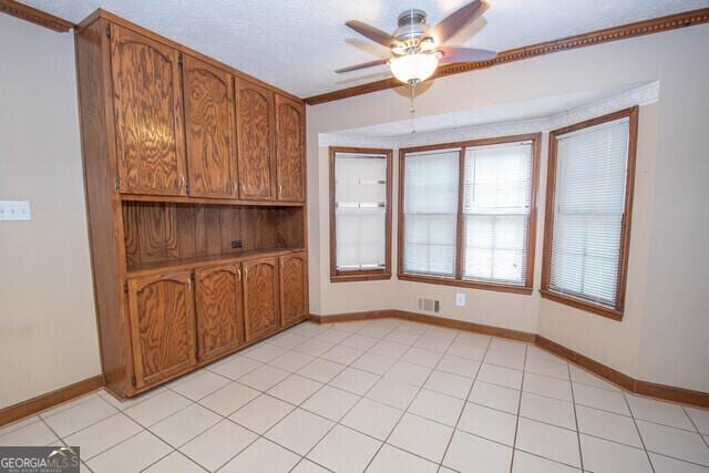 tiled empty room featuring ceiling fan and crown molding