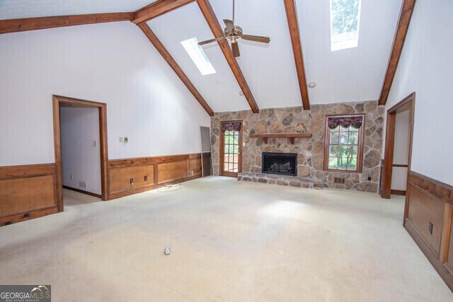 unfurnished living room featuring plenty of natural light, a fireplace, high vaulted ceiling, and a skylight