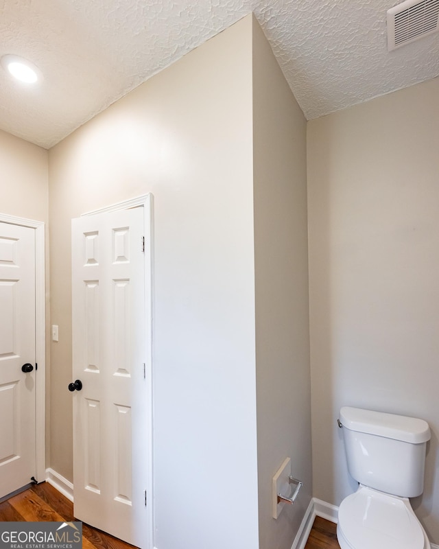 bathroom with wood-type flooring, a textured ceiling, and toilet