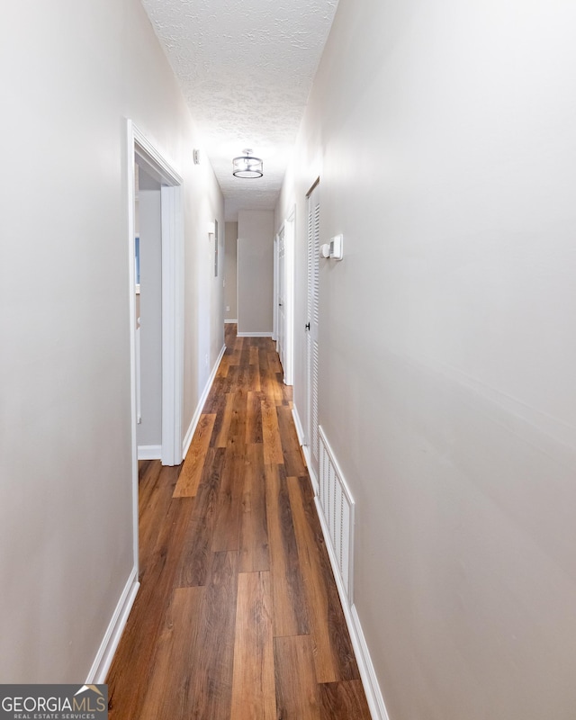 hallway with a textured ceiling and dark wood-type flooring