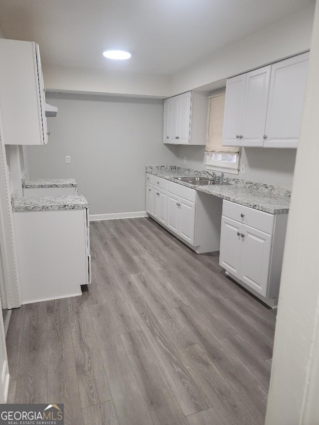 kitchen with white cabinetry, light hardwood / wood-style flooring, light stone countertops, and sink