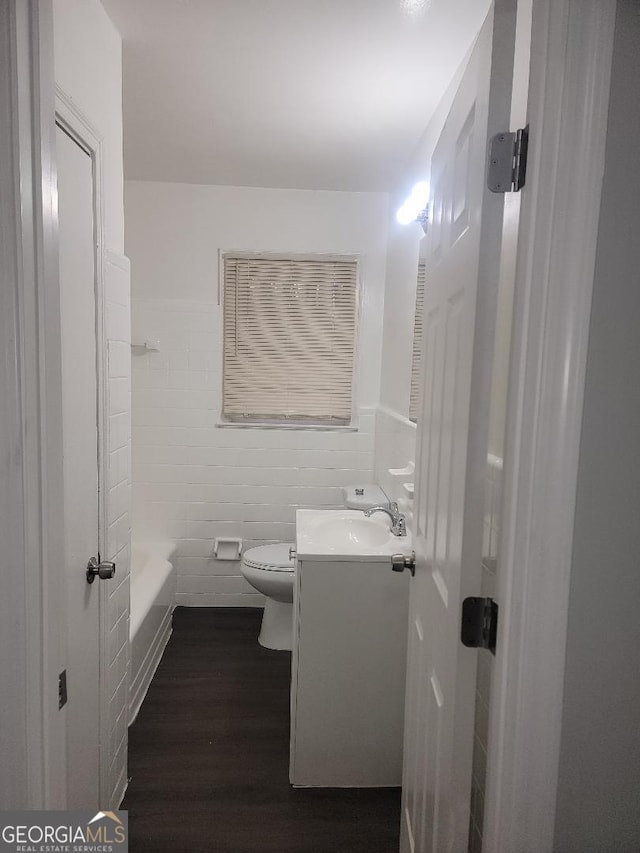 bathroom featuring wood-type flooring, vanity, toilet, and tile walls