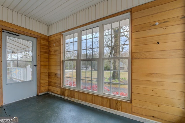 doorway with a wealth of natural light, concrete flooring, and wood walls