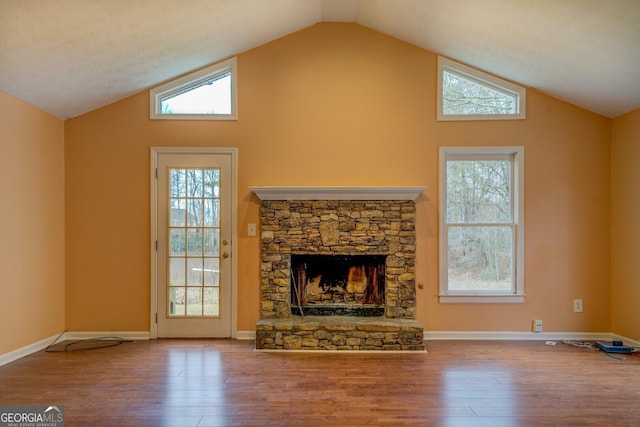 living room with lofted ceiling, a stone fireplace, wood finished floors, and baseboards