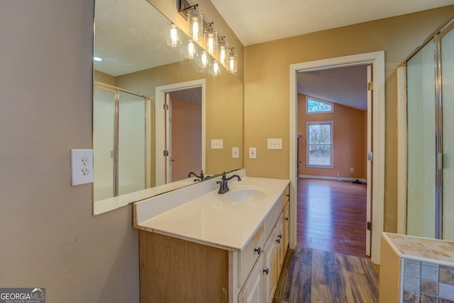 bathroom with a shower with shower door, vaulted ceiling, vanity, and wood finished floors