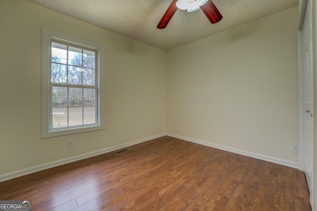 unfurnished room featuring a ceiling fan, baseboards, visible vents, and wood finished floors