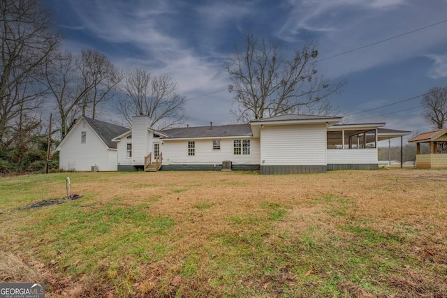 back of house featuring entry steps, a lawn, a chimney, and a sunroom