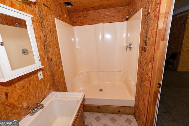 full bathroom featuring a sink, wooden walls, and walk in shower