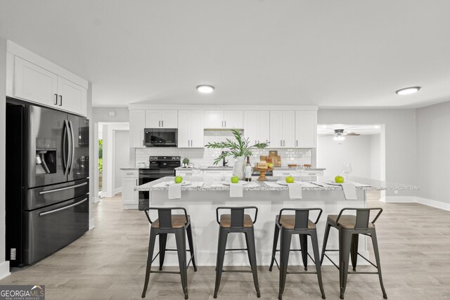 kitchen with a breakfast bar area, decorative backsplash, white cabinetry, and appliances with stainless steel finishes