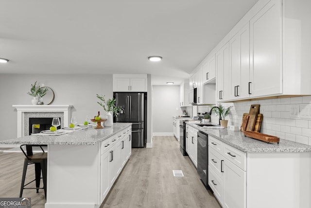 kitchen with light stone countertops, decorative backsplash, a breakfast bar, white cabinets, and appliances with stainless steel finishes