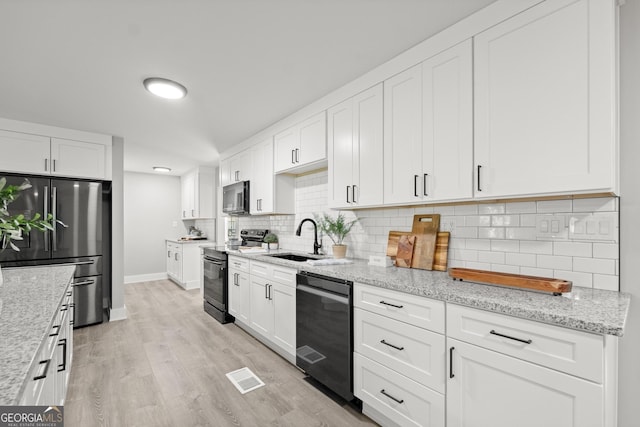 kitchen with black appliances, sink, light stone countertops, light wood-type flooring, and white cabinetry