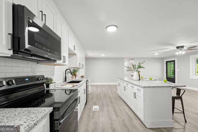 kitchen with a breakfast bar, black electric range, light stone countertops, light hardwood / wood-style floors, and white cabinetry