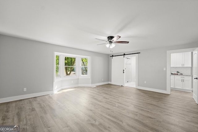 unfurnished living room with a barn door, ceiling fan, and light hardwood / wood-style floors