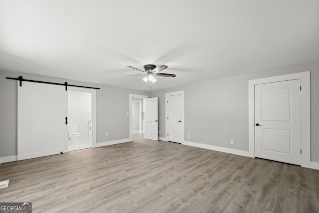 unfurnished bedroom featuring a barn door, light hardwood / wood-style floors, ensuite bath, and ceiling fan