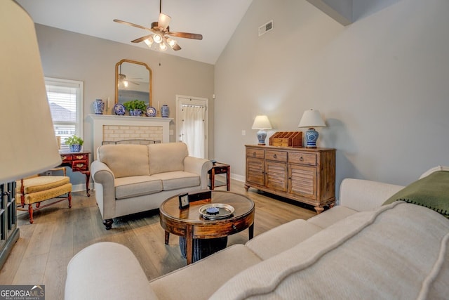 living room with high vaulted ceiling, a brick fireplace, wood finished floors, and visible vents